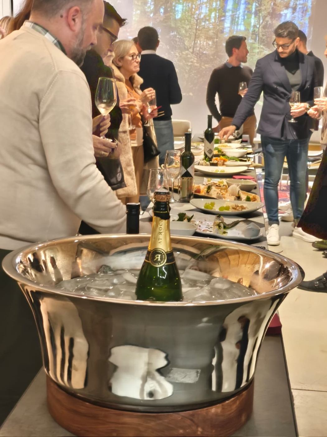Espumoso en una cubitera con invitados brindando al fondo